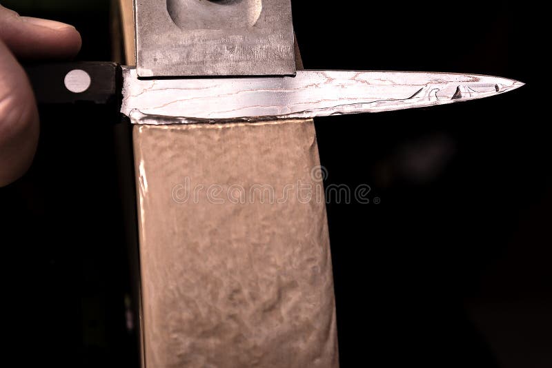 Apontando uma faca de aço de Damasco em uma mó da água imagem de stock Apontando uma faca de aço de Damasco em uma mó da água imagem de stock