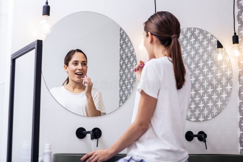 Appealing woman brushing teeth in front of circular mirror