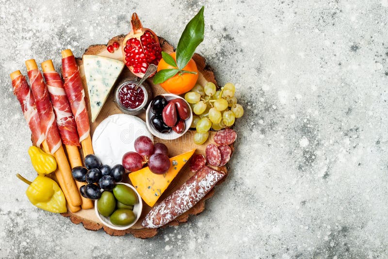 Appetizers table with antipasti snacks. Cheese and meat variety board over grey concrete background. Top view, flat lay.