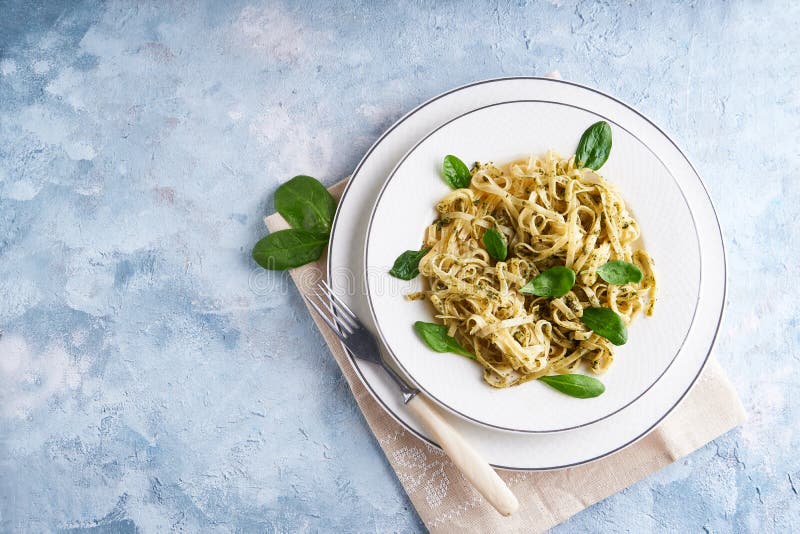 Appetizing Pasta with Sauce Pesto and Spinach in Plate on Light Blue