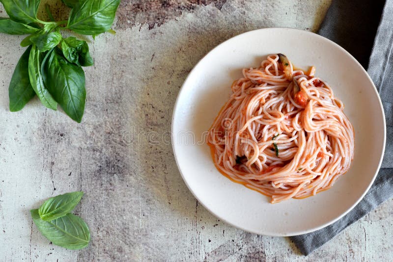 Appetizing pasta with tomatoes, spices and eggplants on a beautiful plate and sprigs of fresh Basil on a gray background royalty free stock image