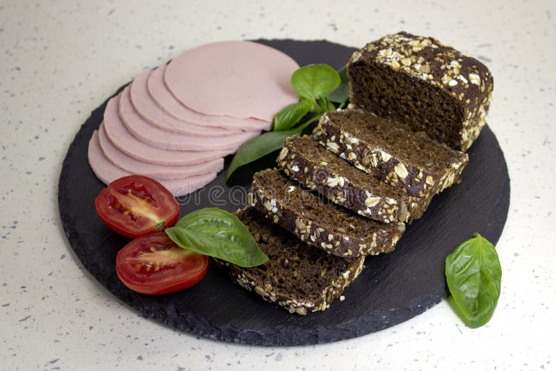 Appetizing sausage  bologne sliced on a slate board on a light marble background with tomatoes and basil  close up