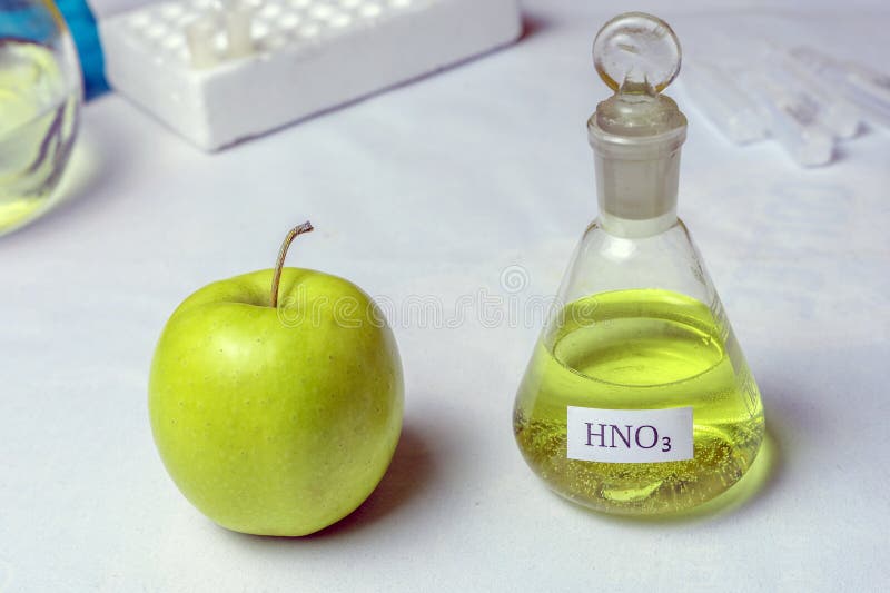 An apple and a chemical flask labeled nitric acid - nitrate. The concept of the presence of nitrates and GMOs