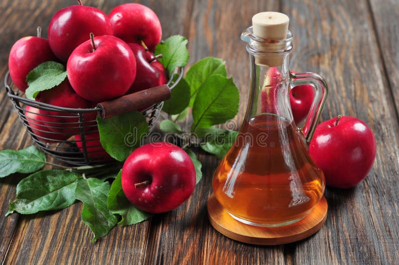 Aceto di sidro di mele in bottiglia di vetro e un cesto con mele fresche.