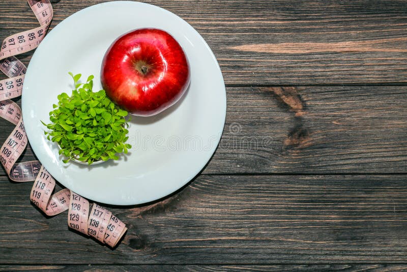 An apple with microgreen on an empty white plate with a tape measure to measure the figure. Diet and raw food concept.