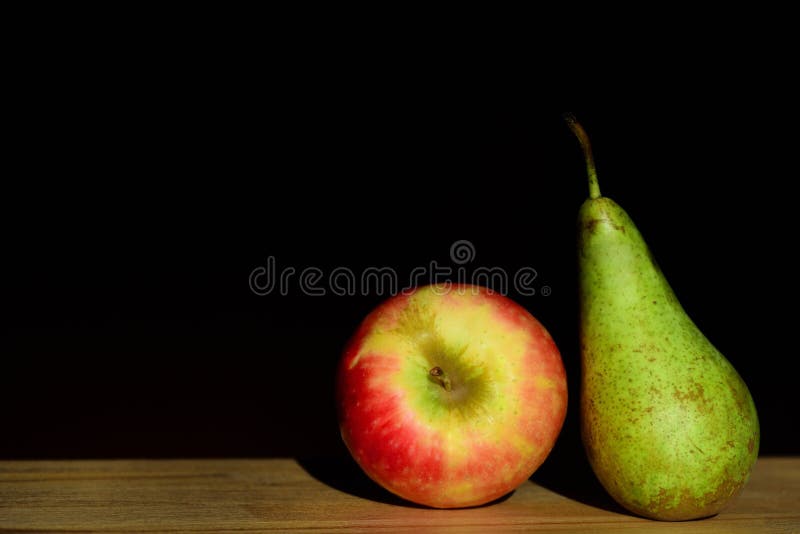 An apple and a pear lie next to each other on a table against a dark background in Germany