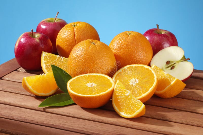 Fresh apples and oranges on a slatted table against a blue sky