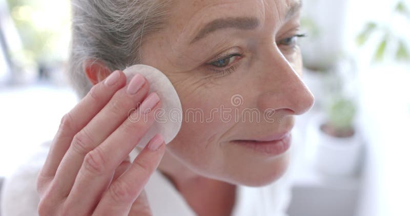Application du produit de soins de la peau femme mature visage nettoyant doucement avec coton tampon à la maison banque de vidéos