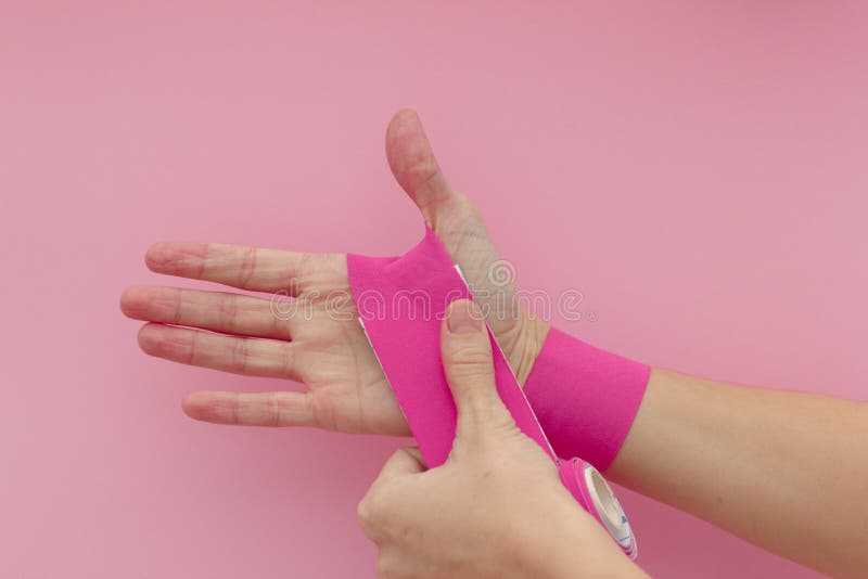 Appling a Kinesio Tape To Hand Isolated on Pink Background. Physiotherapy Tape for Wrist Pain, Aches and Tension Stock Photo - of equipment: 170526420