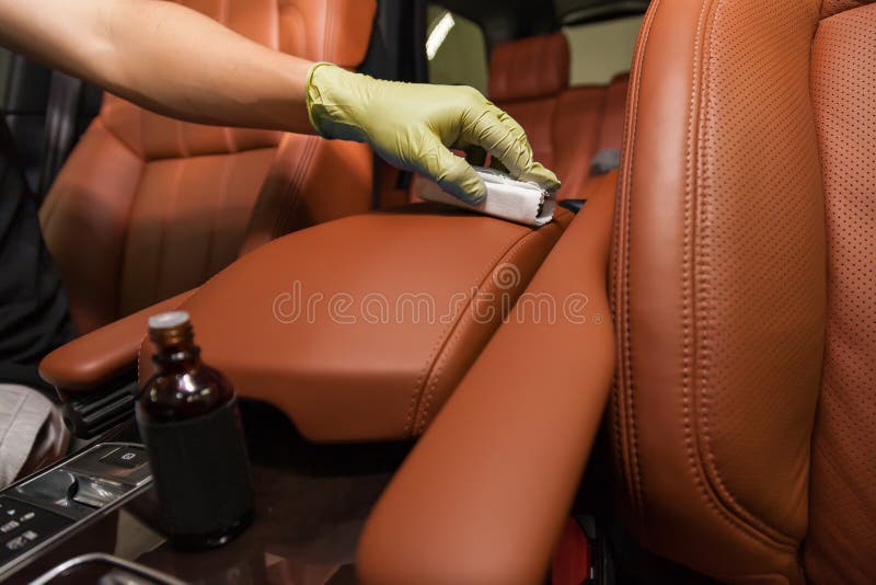 Applying a nano-ceramic coating for interior leather on the car`s seat brown upholstery by a worker in yellow gloves with a spong