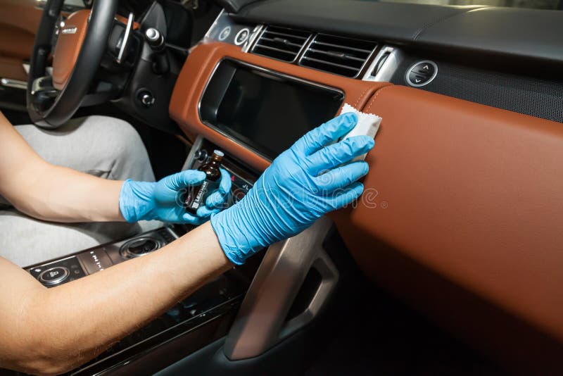 Applying a nano-ceramic coating for interior Ceramic Pro Leather 9h and Light on the car`s dashboard brown upholstery by a worker