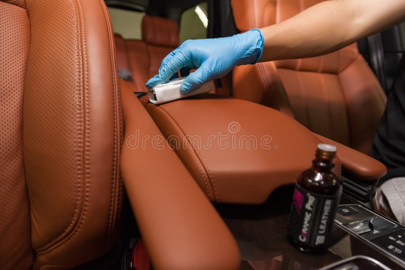 Applying a nano-ceramic coating for interior Ceramic Pro Leather 9h and Light on the car`s seat brown upholstery by a worker with