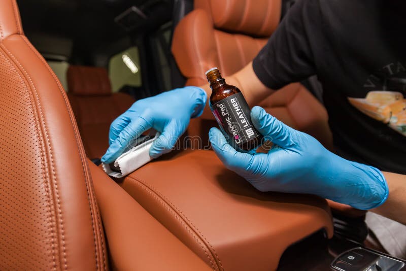 Applying a nano-ceramic coating for interior Ceramic Pro Leather 9h and Light on the car`s seat brown upholstery by a worker with