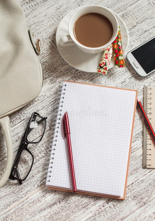 Apra un taccuino, una penna, una borsa delle donne, un telefono, un righello, una matita e una tazza di caffè bianchi in bianco fotografia stock Apra un taccuino, una penna, una borsa delle donne, un telefono, un righello, una matita e una tazza di caffè bianchi in bianco fotografia stock