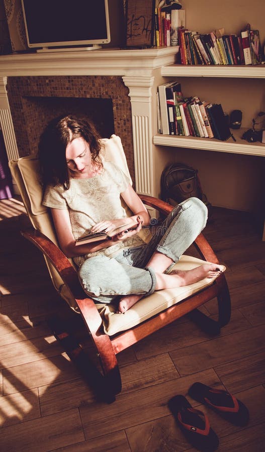Apreciando o tempo em casa Mulher que relaxa na cadeira moderna confortável que lê o livro de papel Luz natural HOME acolhedor Ap fotos de stock Apreciando o tempo em casa Mulher que relaxa na cadeira moderna confortável que lê o livro de papel Luz natural HOME acolhedor Ap fotos de stock