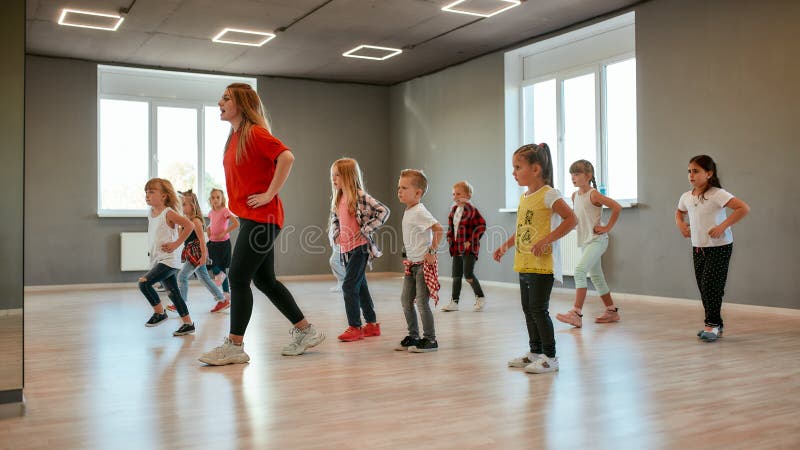 Group of little boys and girls dancing while having choreography class in the dance studio. Female dance teacher and children. Contemp dance. Hip hop. Kids and sport. Full length. Group of little boys and girls dancing while having choreography class in the dance studio. Female dance teacher and children. Contemp dance. Hip hop. Kids and sport. Full length