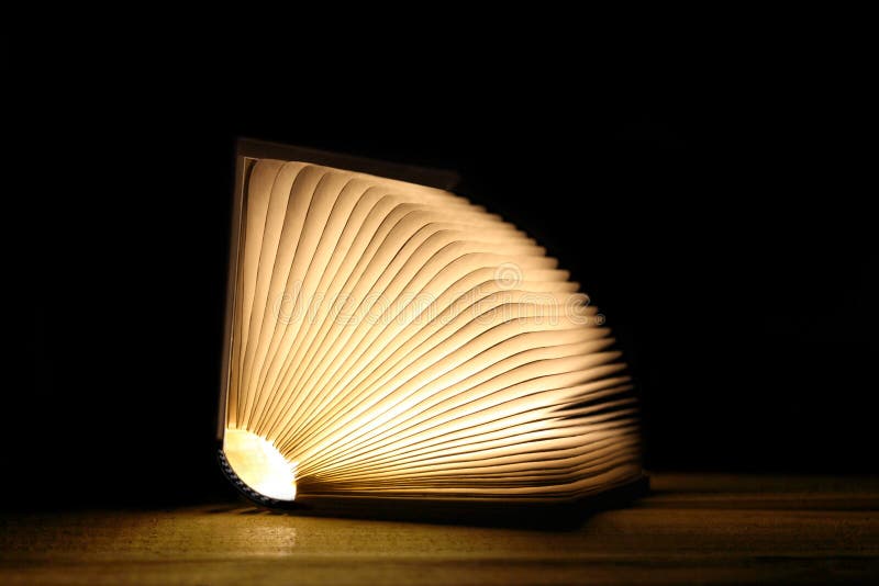 Apri libro magico con pagine luminose su una tabella di legno e sfondo nero con spazio di copia per il testo immagine stock libera da diritti