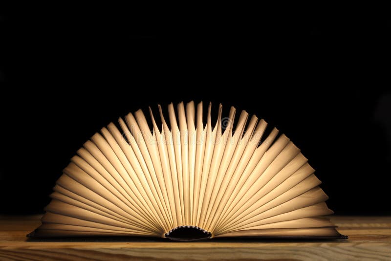 Apri libro magico con pagine luminose su una tabella di legno e sfondo nero con spazio di copia per il testo immagine stock