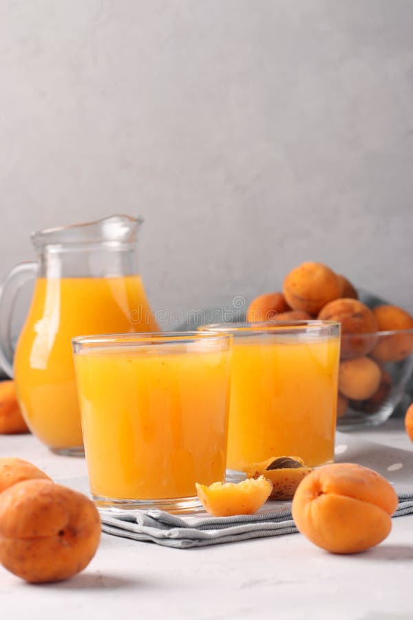 Apricot juice with pulp in two glasses and a jug on a gray background, Closeup