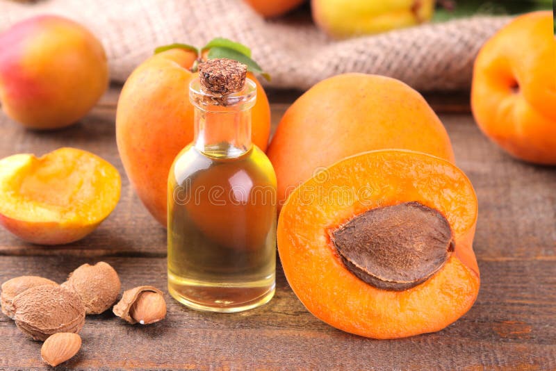 Apricot seed oil next to apricots on a brown background