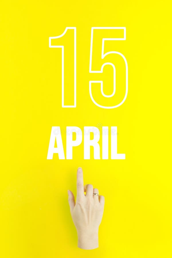 April 15th. Day 15 of month, Calendar date. Hand finger pointing at a calendar date on yellow background. Spring month, day of the stock photo