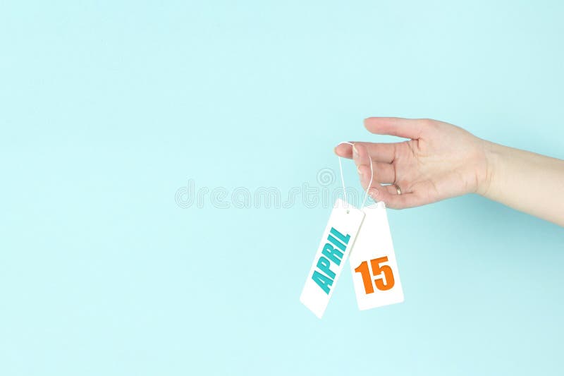 April 15th. Day 15 of month, Calendar date. Hand hold price tag with calendar date on blue background. Spring month, day of the stock image