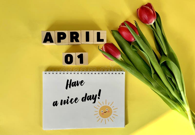 April 1 on wooden cubes on a yellow background.Next to a bouquet of tulips and a notebook with the inscription have a nice day .