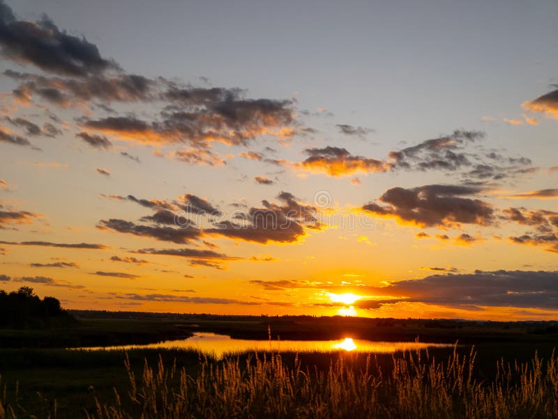 Apus de soare peste un lac cu iarbă înaltă în prim-plan stock photography