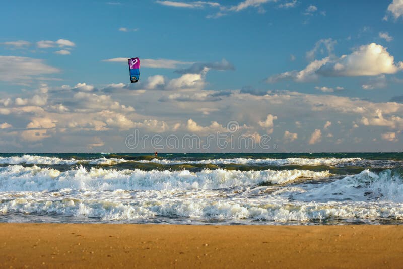 Aquilone di giri di Kitesurfer attraverso le onde praticanti il surfing del mare tempestoso alla spiaggia sabbiosa al tramonto da immagine stock libera da diritti Aquilone di giri di Kitesurfer attraverso le onde praticanti il surfing del mare tempestoso alla spiaggia sabbiosa al tramonto da immagine stock libera da diritti
