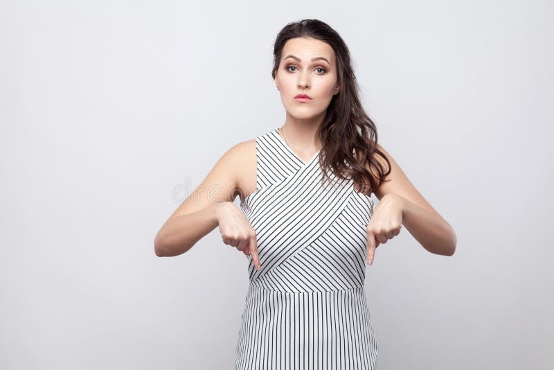 Aquí y a la derecha sepa Retrato de la mujer morena joven hermosa seria con la situación rayada del vestido y de mirar la cámara foto de archivo libre de regalías Aquí y a la derecha sepa Retrato de la mujer morena joven hermosa seria con la situación rayada del vestido y de mirar la cámara foto de archivo libre de regalías