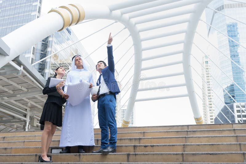 Arab businessman holding blueprint on hand and talk about construction process with Asian businessman and businesswoman stock photos Arab businessman holding blueprint on hand and talk about construction process with Asian businessman and businesswoman stock photos
