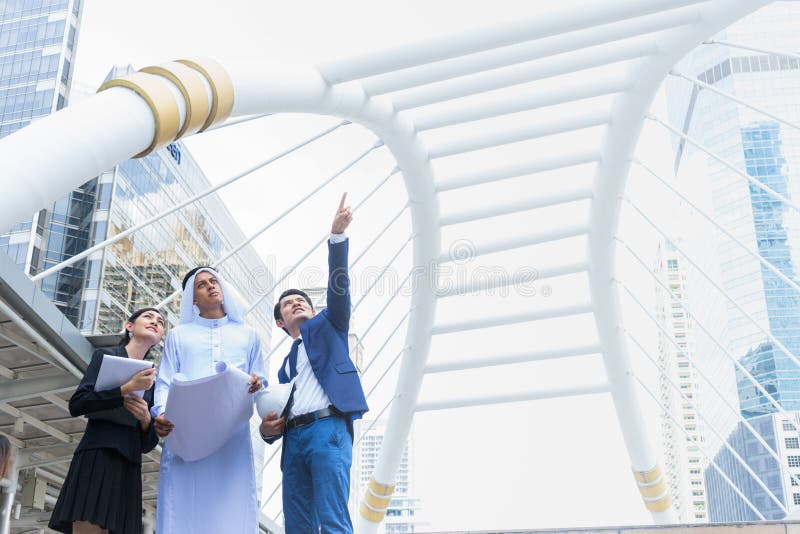 Arab businessman holding blueprint on hand and talk about construction process with Asian businessman and businesswoman in the stock photography Arab businessman holding blueprint on hand and talk about construction process with Asian businessman and businesswoman in the stock photography