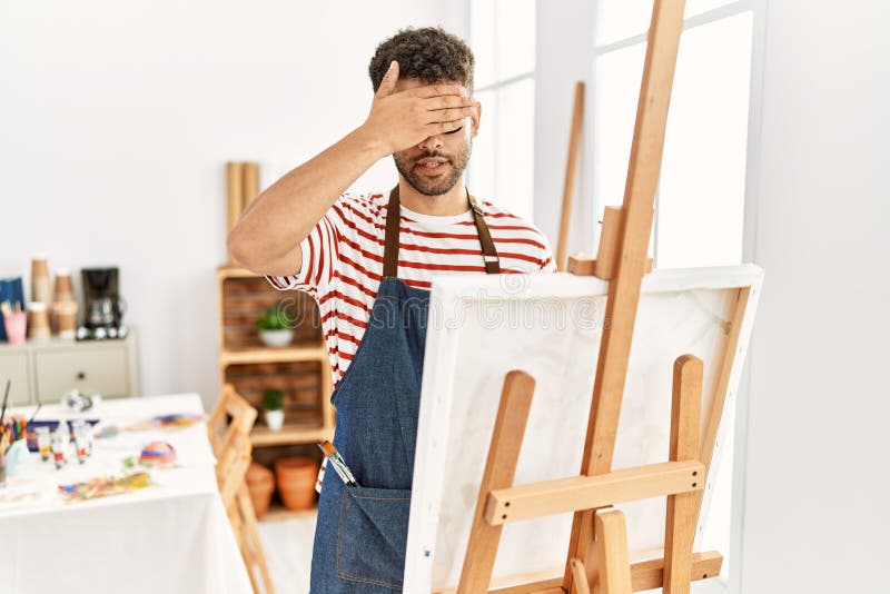 Arab young man at art studio smiling and laughing with hand on face covering eyes for surprise. blind concept. Arab young man at art studio smiling and laughing with hand on face covering eyes for surprise. blind concept