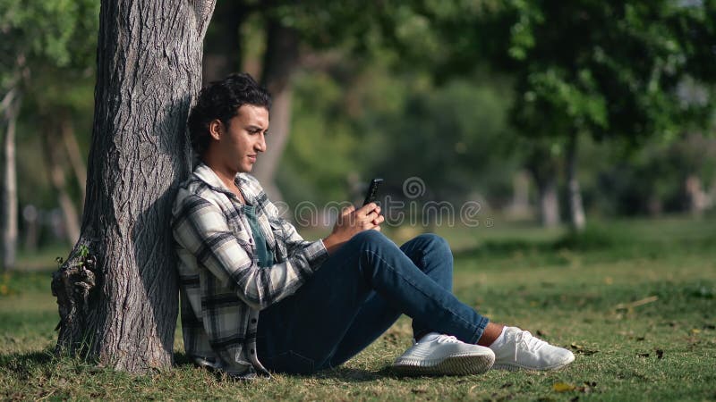 Arabic modern man use smartphone sitting near tree summer sunny park enjoy weekend outdoor leisure stock video
