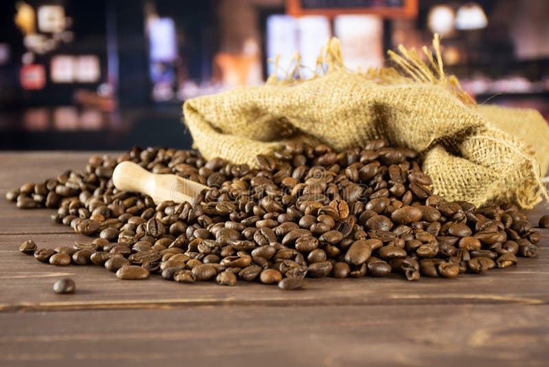 Lot of whole dark brown coffee beans sweet arabica variety in a jute bag with restaurant in background. Lot of whole dark brown coffee beans sweet arabica variety in a jute bag with restaurant in background