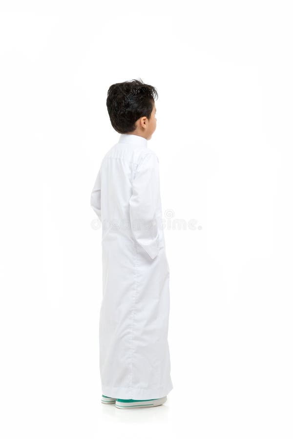 Arabska chłopiec patrzeje tło z ręką w jego wkładać do kieszeni, będący ubranym białego tradycyjnego saudyjczyka Thobe i sneakers