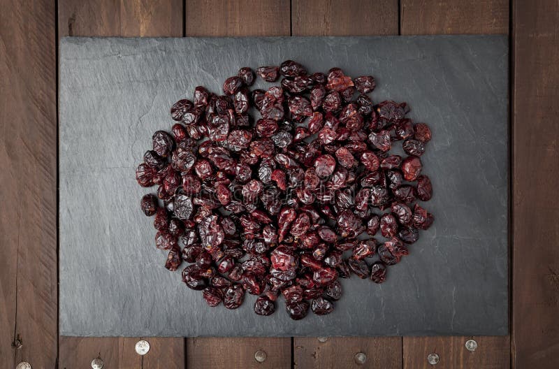 Dry red cranberries on a square shaped slate plate on a brown wooden table. Dry red cranberries on a square shaped slate plate on a brown wooden table.