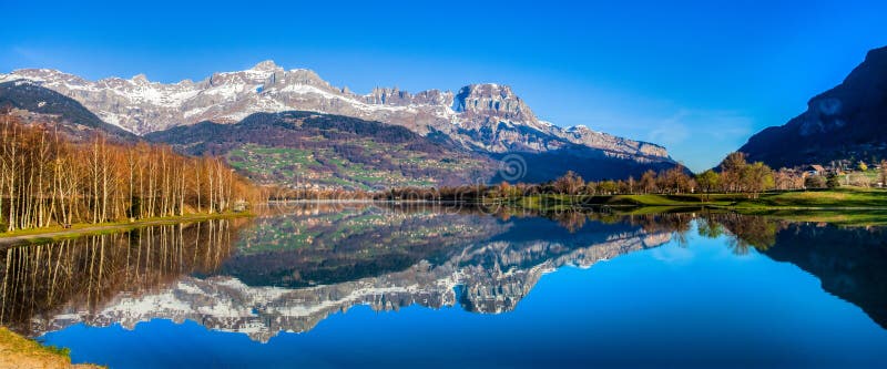 Panoramic view of Aravis mountain range reflected clearly on the surface of the surface of Lac du Passy, Passy, France. Located in the Arve Valley, France, between Geneva, Switzerland and Chamonix, Mont Blanc. Panoramic view of Aravis mountain range reflected clearly on the surface of the surface of Lac du Passy, Passy, France. Located in the Arve Valley, France, between Geneva, Switzerland and Chamonix, Mont Blanc.