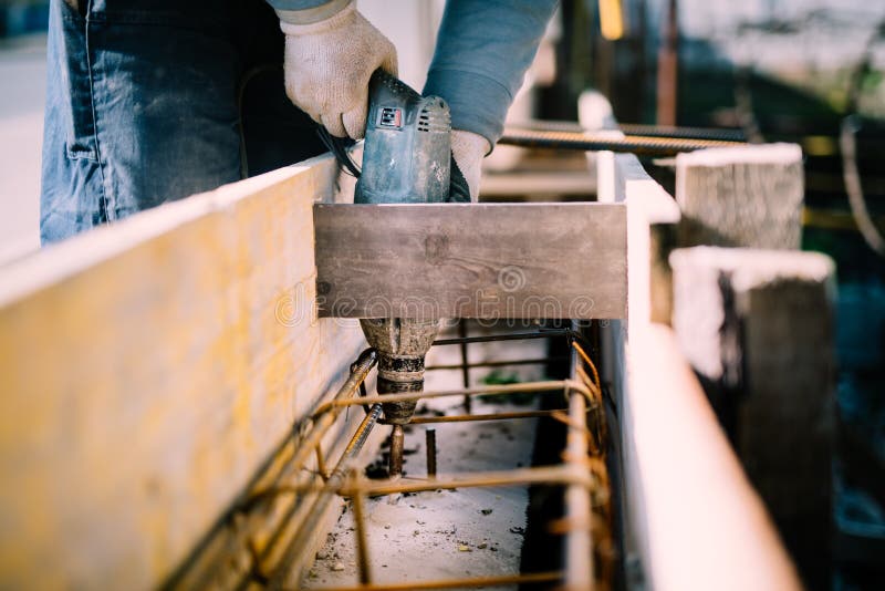 Arbeider gebruikend een hulpmiddel van de boormacht op bouwwerf en creërend gaten in cement voor stichtingsversterking royalty-vrije stock afbeelding Arbeider gebruikend een hulpmiddel van de boormacht op bouwwerf en creërend gaten in cement voor stichtingsversterking royalty-vrije stock afbeelding