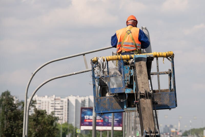 Arbeider in liftemmer tijdens installatie van metaalpool met straatlantaarn, straatlantaarnpool met dubbel hoofd stock afbeeldingen Arbeider in liftemmer tijdens installatie van metaalpool met straatlantaarn, straatlantaarnpool met dubbel hoofd stock afbeeldingen