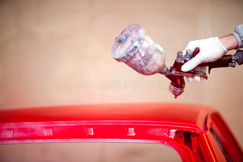 Werknemer schildert met de hand de motorkap van een auto in een autowerkplaats stock afbeelding