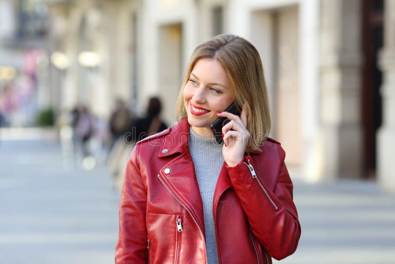 Front view portrait of a fashion blonde calling on phone and looking at side walking towards camera on the street. Front view portrait of a fashion blonde calling on phone and looking at side walking towards camera on the street