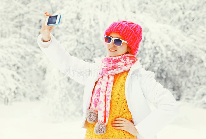 Arbeiten Sie die Winterfrau um, die Bildselbstporträt auf Smartphone über den schneebedeckten Bäumen nimmt, die einen bunten Stri lizenzfreie stockfotos