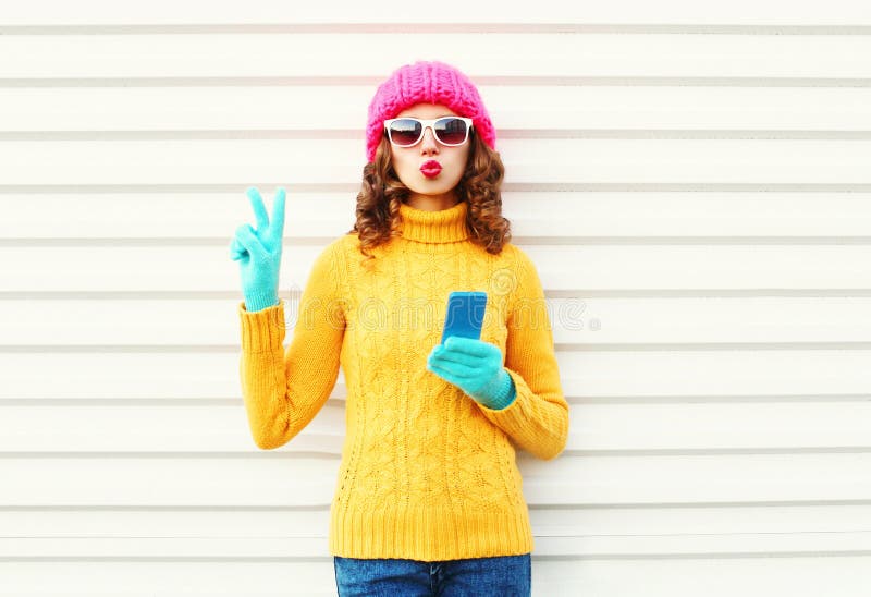 Arbeiten Sie recht junge Frau mit dem Smartphone um, der bunte gestrickte Kleidung über Weiß trägt stockfotografie