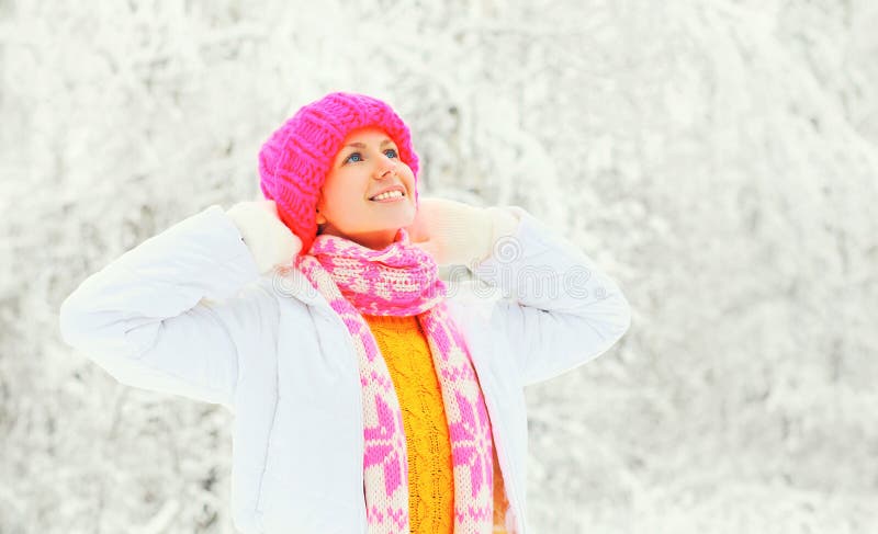 Arbeiten Sie Winterporträt die glückliche Frau um, die einen bunten Strickmützestrickjackenschal über schneebedecktem Hintergrund stockfotografie