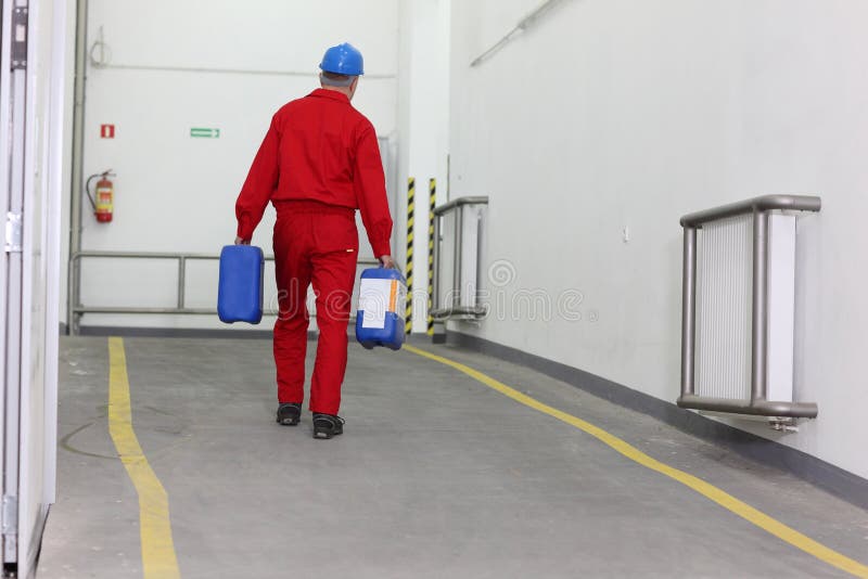 Back view of a factory worker carrying 2 bottles of chemicals/materials in a factory. Back view of a factory worker carrying 2 bottles of chemicals/materials in a factory.