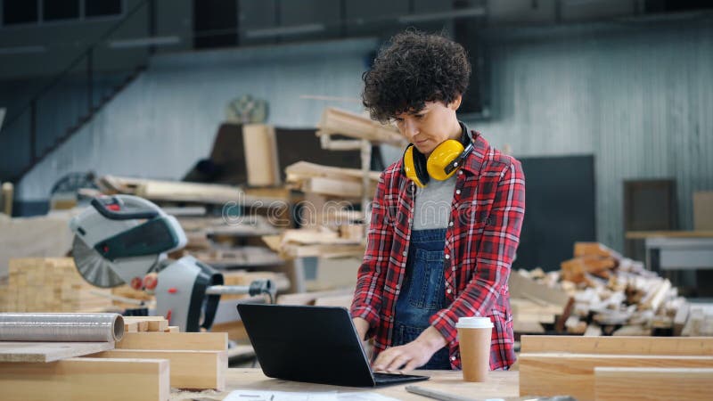 Arbeitnehmerin, die Laptop in Schreibenstellung der hölzernen Werkstatt an Arbeitsplatz allein verwendet