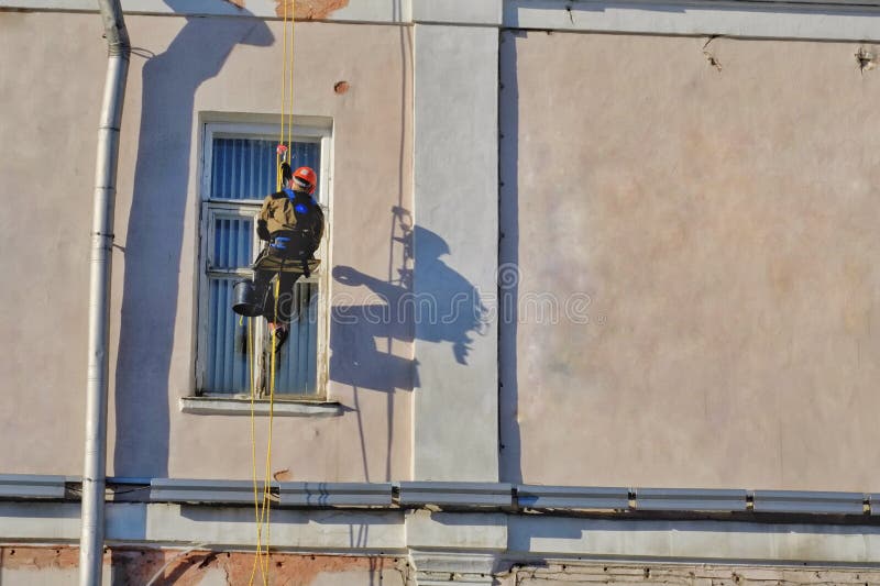 Arbeitskraft, die an der Baustelle mit Sturzhelm und an der Uniform für Arbeiten auf Höhe außerhalb des Gebäudes klettert stockbilder Arbeitskraft, die an der Baustelle mit Sturzhelm und an der Uniform für Arbeiten auf Höhe außerhalb des Gebäudes klettert stockbilder