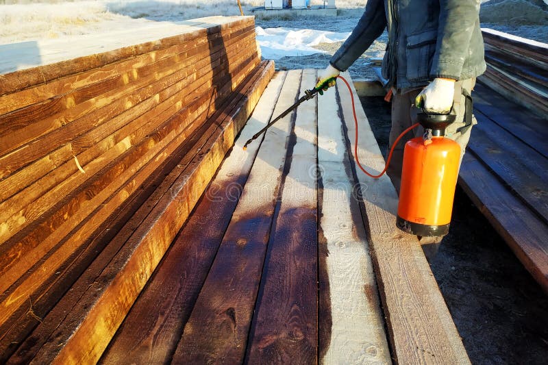 arbetaren besprutar en brun målarfärg på brädena på gatan arkivfoton arbetaren besprutar en brun målarfärg på brädena på gatan arkivfoton