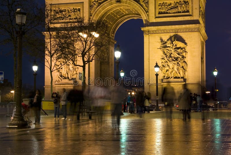 Tightly-framed photograph of the Arc De Triomphe taken at night with blurred figures in the foreground. Tightly-framed photograph of the Arc De Triomphe taken at night with blurred figures in the foreground.